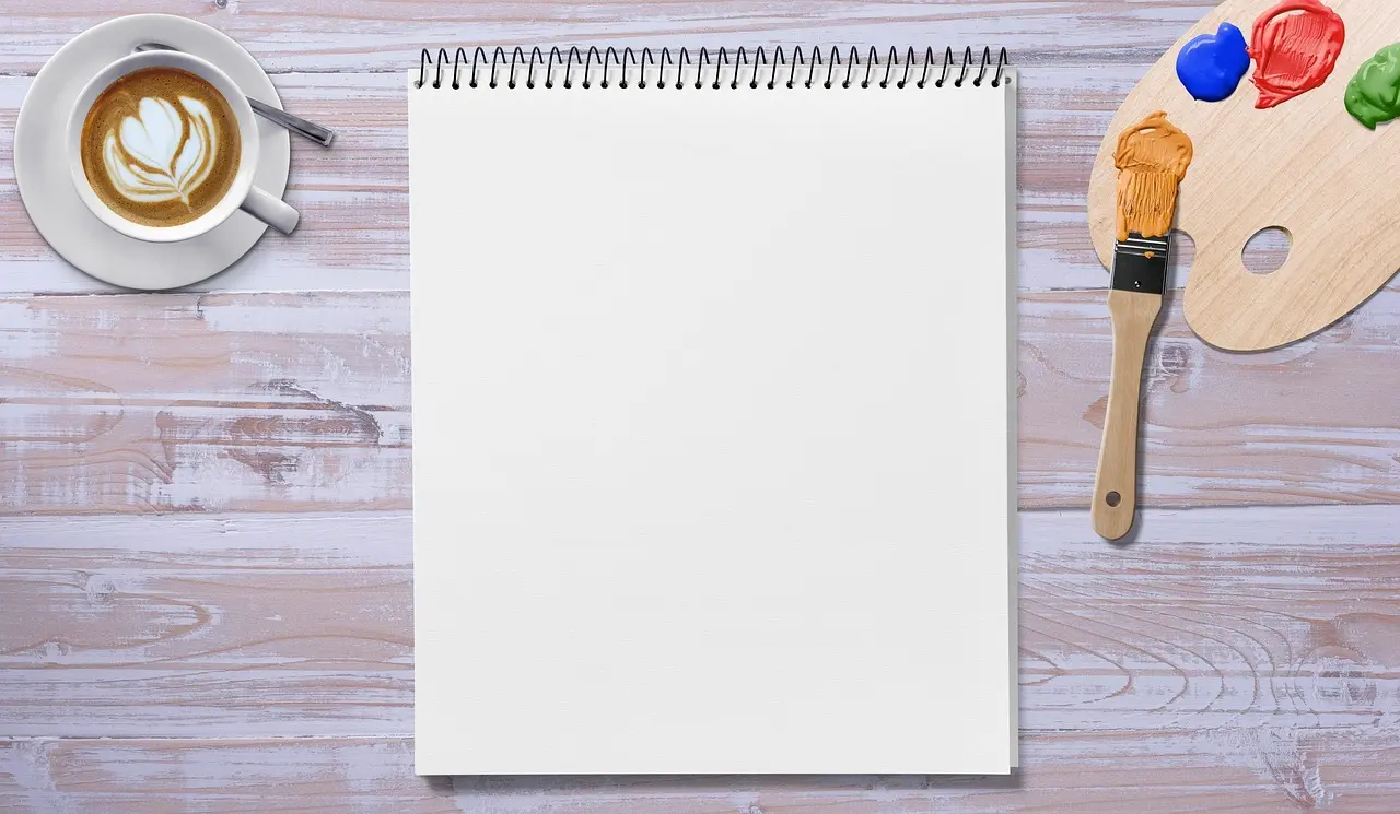 Noteblok på træbord med kaffe, pensel og farvepalet